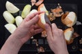 Top view of woman hands peeling off with knife cutted in half unpeeled onion on the black background