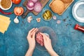 Top view of woman holding bawl with raw minced meat near fresh burger ingredients on blue textured surface