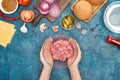 Top view of woman holding bawl with raw minced meat near fresh burger ingredients on blue textured surface