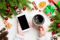 Top view of a woman holding a cup of coffee in one hand and a phone in another hand on wooden background. Fir tree and Christmas Royalty Free Stock Photo