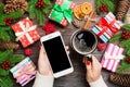 Top view of a woman holding a cup of coffee in one hand and a phone in another hand on wooden background. Fir tree and Christmas Royalty Free Stock Photo