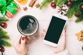 Top view of a woman holding a cup of coffee in one hand and a phone in another hand on wooden background. Fir tree and Christmas Royalty Free Stock Photo