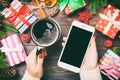 Top view of a woman holding a cup of coffee in one hand and a phone in another hand on wooden background. Fir tree and Christmas Royalty Free Stock Photo