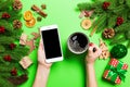 Top view of a woman holding a phone in one hand and a cup of coffee in another hand on green background. Christmas decorations and Royalty Free Stock Photo