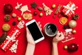 Top view of a woman holding a phone in one hand and a cup of coffee in another hand on red background. Christmas decorations and Royalty Free Stock Photo