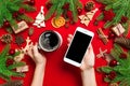 Top view of a woman holding a phone in one hand and a cup of coffee in another hand on red background. Christmas decorations and Royalty Free Stock Photo