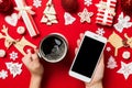 Top view of a woman holding a phone in one hand and a cup of coffee in another hand on red background. Christmas decorations and Royalty Free Stock Photo