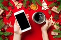 Top view of a woman holding a phone in one hand and a cup of coffee in another hand on red background. Christmas decorations and Royalty Free Stock Photo