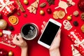 Top view of a woman holding a phone in one hand and a cup of coffee in another hand on red background. Christmas decorations and Royalty Free Stock Photo