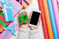 Top view of a woman holding a phone in one hand and a gift in another on wooden background. Rolled up wrapping paper and holiday Royalty Free Stock Photo