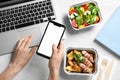 Top view of woman holding smartphone over white wooden table with lunchboxes. Healthy food delivery