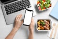 Top view of woman holding smartphone over white wooden table with lunchboxes. Healthy food delivery