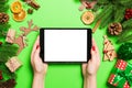 Top view of woman holding tablet in her hands on green background made of Christmas decorations. New Year holiday concept. Mockup Royalty Free Stock Photo