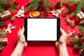 Top view of woman holding tablet in her hands on red background made of Christmas decorations. New Year holiday concept. Mockup Royalty Free Stock Photo