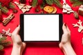 Top view of woman holding tablet in her hands on red background made of Christmas decorations. New Year holiday concept. Mockup Royalty Free Stock Photo