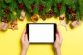 Top view of woman holding tablet in her hands on yellow background made of Christmas decorations. New Year holiday concept. Mockup Royalty Free Stock Photo