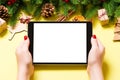 Top view of woman holding tablet in her hands on yellow background made of Christmas decorations. New Year holiday concept. Mockup Royalty Free Stock Photo
