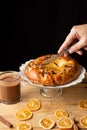 Top view of woman`s hand cutting a chocolate brioche, on wooden table with glass of chocolate and orange slices, vertical, Royalty Free Stock Photo