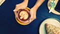 Top view of woman`s hand holding art latte coffee with almond cream croissant, knife, fork and phone on blue wooden background Royalty Free Stock Photo