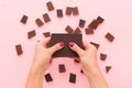 Top view on woman`s hands breaking a piece of dark chocolate above pink table background