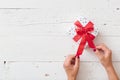 Top view on woman`s hands unwrapping Christmas or birthday gift box with red satin ribbon on white wooden background