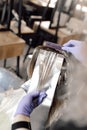 Unrecognizable woman hairdresser colorist hold dyed long hair on foil, brushing with purple barber comb in blue gloves.