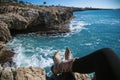 Top view on woman traveler legs sitting on the top of the rock with a beautiful travel view on Mediterranean sea and waves