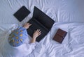 Top view of woman in white bathrobe with shower cap lying down and using laptop computer on her bed Royalty Free Stock Photo