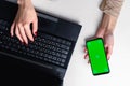 Top view of woman& x27;s hands typing on laptop keypad placed on white office desktop with blank smartphone Royalty Free Stock Photo
