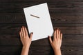 Top view of women`s hands, ready to write something on an empty piece of paper lying on a wooden table. White blank sheet of pape Royalty Free Stock Photo