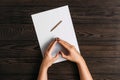 Top view of women`s hands, ready to write something on an empty piece of paper lying on a wooden table. White blank sheet of pape Royalty Free Stock Photo