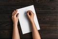 Top view of women`s hands, ready to write something on an empty piece of paper lying on a wooden table. White blank sheet of pape Royalty Free Stock Photo