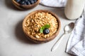 Top view on a wooden bowl with freshly prepared granola or oatmeal granola with blueberries, a glass of milk nearby. Healthy