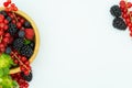 Top view of the wooden bowl on the left of the image with strawberries, redcurrants, blueberries, blackberries and raspberries