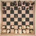Top view on wooden chess board with chess figures ready for the game and man's hand making chess move on white wooden table Royalty Free Stock Photo