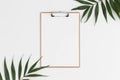 Top view of a wooden clipboard mockup with palm leaf decoration on a white table