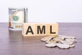 top view of wooden cubes with text AML over US dollar banknotes and coins on a brown wooden background Royalty Free Stock Photo