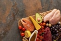 Top view of wooden cutting board with raw fish, meat, poultry, cheese, fruits, vegetables, olive oil and peanuts on dark Royalty Free Stock Photo
