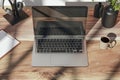 Top view of wooden designer desk with reflections on laptop screen, coffee cup, supplies and other items.