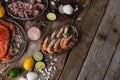 Top view of the wooden rustic table with plates with seafood served by lime, lemon, sea salt, spices and seashells. Cooked king