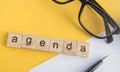 Top view the word of the agenda written on wooden cubes on the desktop with glasses  pen  paper Notepad on a yellow background Royalty Free Stock Photo