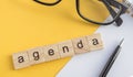 Top view the word of the agenda written on wooden cubes on the desktop with glasses  pen  paper Notepad on a yellow background Royalty Free Stock Photo