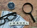 Top view word travel with compass, eye glasses, fake money and magnifier on world map.