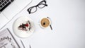 Top view of work place table, laptop with glasses notebook, cake and cup of coffee on white background