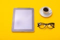 Working space with tablet, glasses and cup of coffee in morning isolated on yellow background Royalty Free Stock Photo