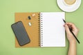 Top view of working table. Open notebook, coffee cup, smartphone and a woman hand holding an pencil, writting a message. Copy