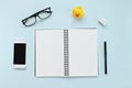 Top view of workspace desk with blank notebook, eye glasses, smart phone, duck and office stationery on blue background Royalty Free Stock Photo