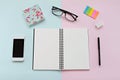 Top view of workspace desk with blank notebook, eye glasses, smart phone and office stationery on pink and blue background Royalty Free Stock Photo
