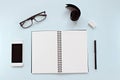 Top view of workspace desk with blank notebook, eye glasses, smart phone, ribbon and office stationery on blue background Royalty Free Stock Photo