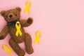 Top view of yellow awareness ribbons and teddy bear on pink background, international childhood cancer day concept.